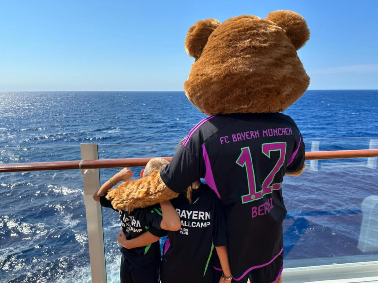 Ein großer Teddybär umarmt zwei Kinder auf einem Schiff