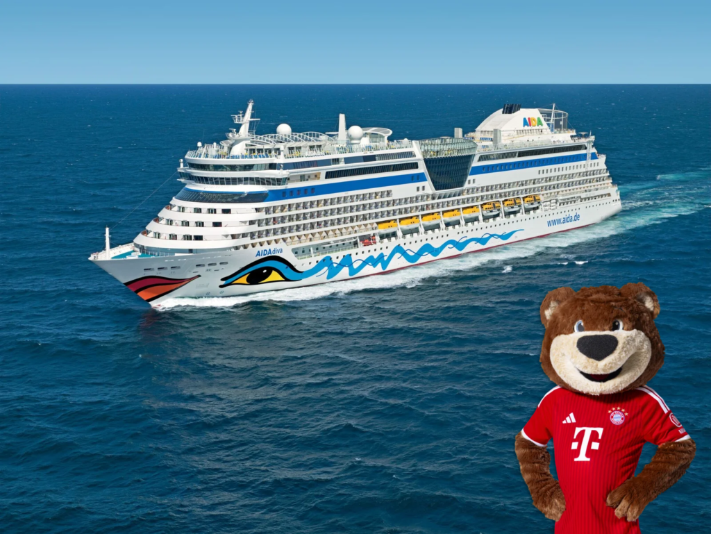 Kreuzfahrtschiff von AIDA Cruises auf dem Meer bei Sonnenuntergang, im Vordergrund rechts ein Plüschmaskottchen im roten FC-Bayern-Trikot.