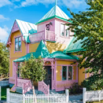 Pinkes Haus mit grünem Dach, umgeben von einem weißen Zaun.